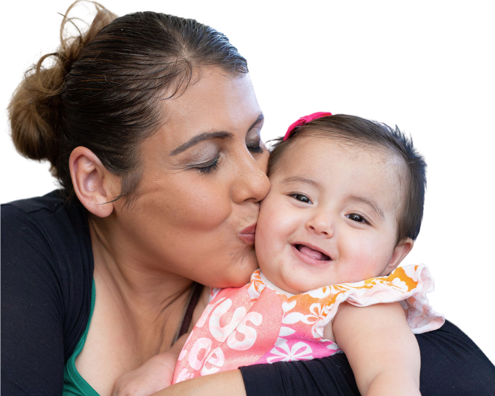 Image of YWCA program participants. Mom kissing smiling young baby in a flowery dress.